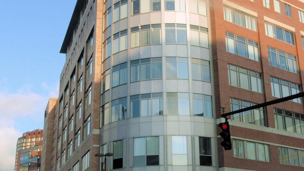 A multistory brick and glass office building on a Cambridge street corner with a traffic signal in the foreground.