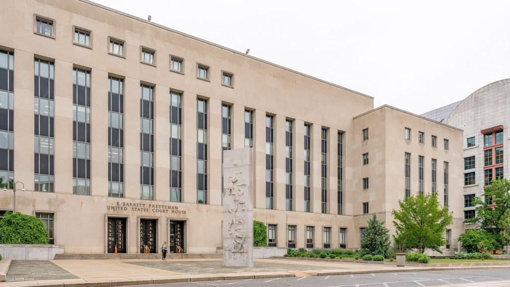 The stone facade of a large federal courthouse building in Washington, D.C., under a clear sky.