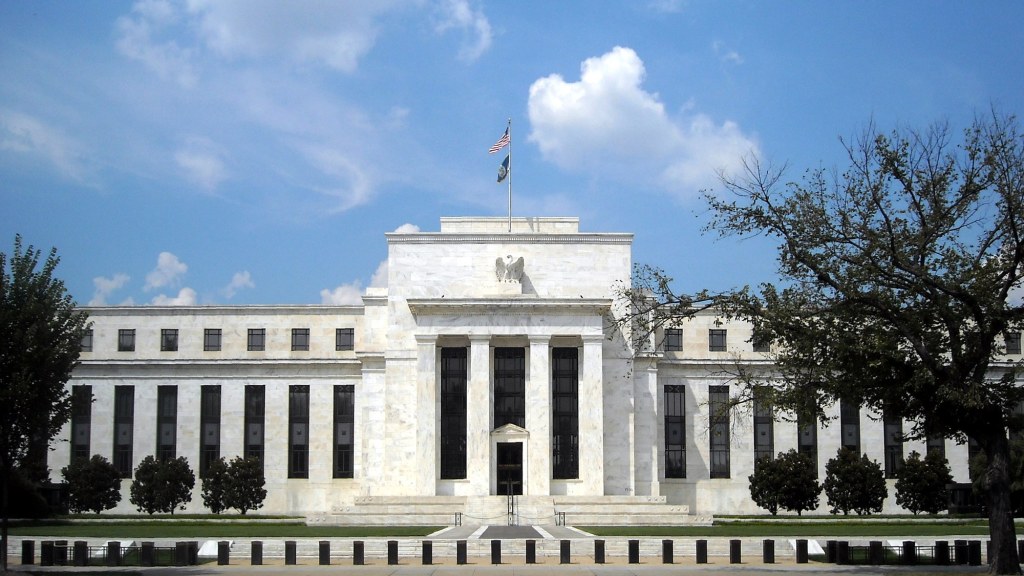 The white marble facade of the Federal Reserve's headquarters building behind a lawn.