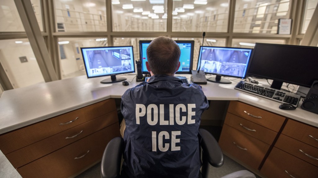 An ICE officer seated at a monitoring station inside a detention facility.