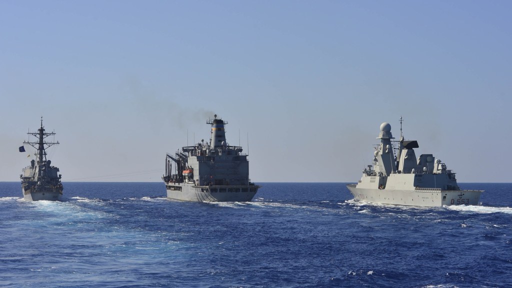 A gray Italian Navy destroyer with the hull number D 553 sails close alongside another ship at sea.