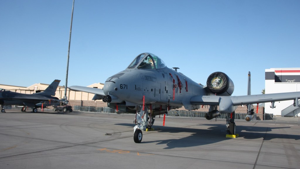 A gray A-10 attack jet with its large nose-mounted cannon parked on an airfield ramp.