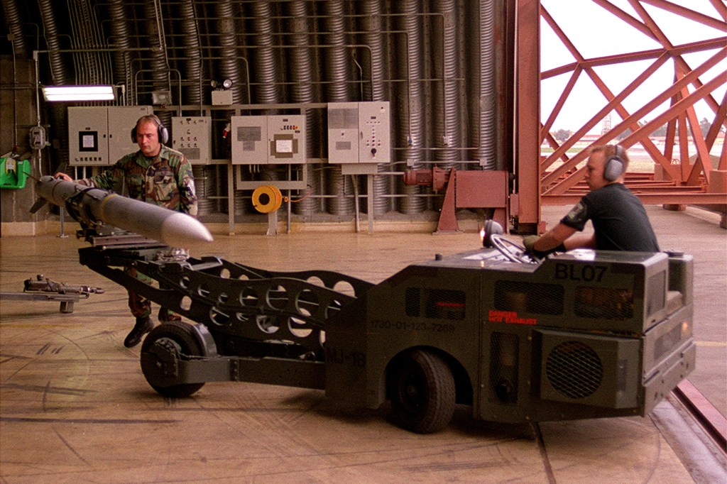 Two U.S. Air Force airmen transport a long AIM-120 AMRAAM missile on a weapons cart beside an F-15C.