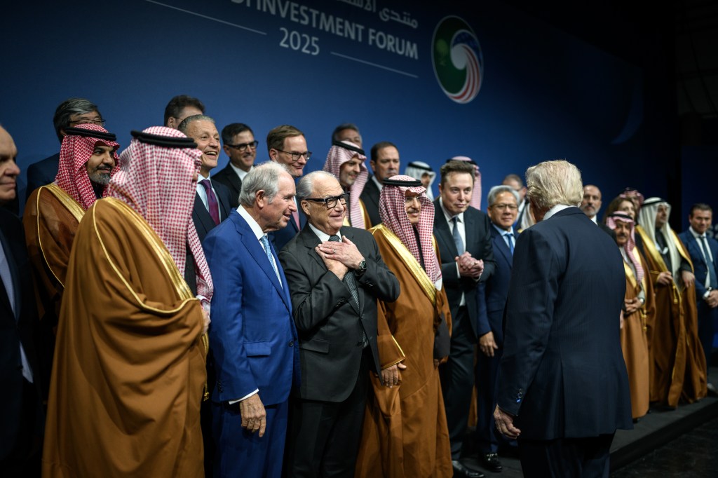 President Donald Trump approaches Elon Musk, Jensen Huang and other executives on stage at an investment forum.