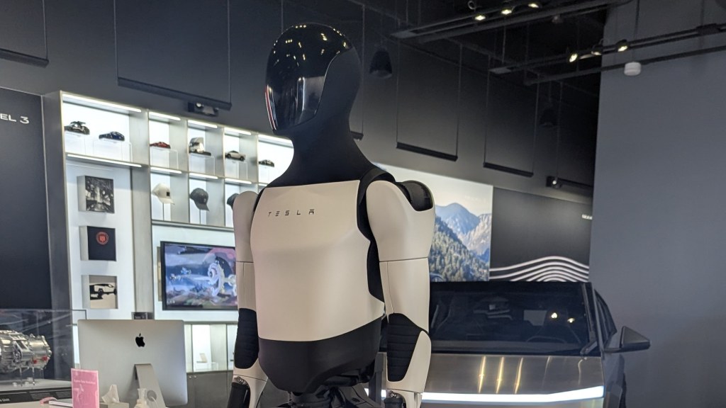 A white and black Tesla Optimus humanoid robot standing in a car showroom.