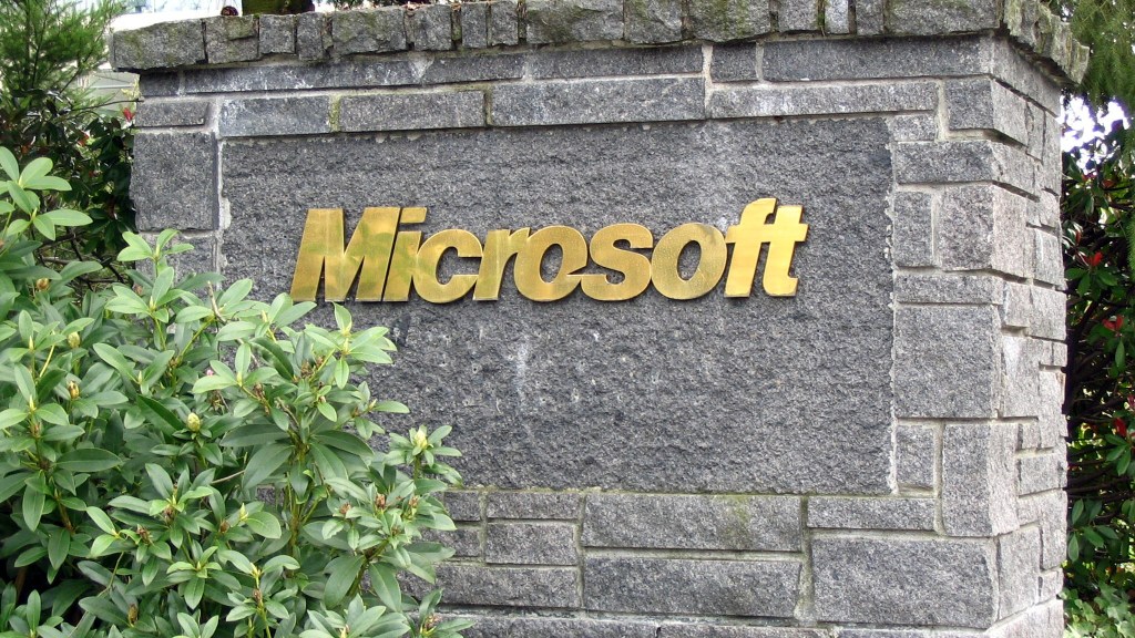 Gold Microsoft lettering on a gray stone sign at a campus entrance, framed by green shrubs.