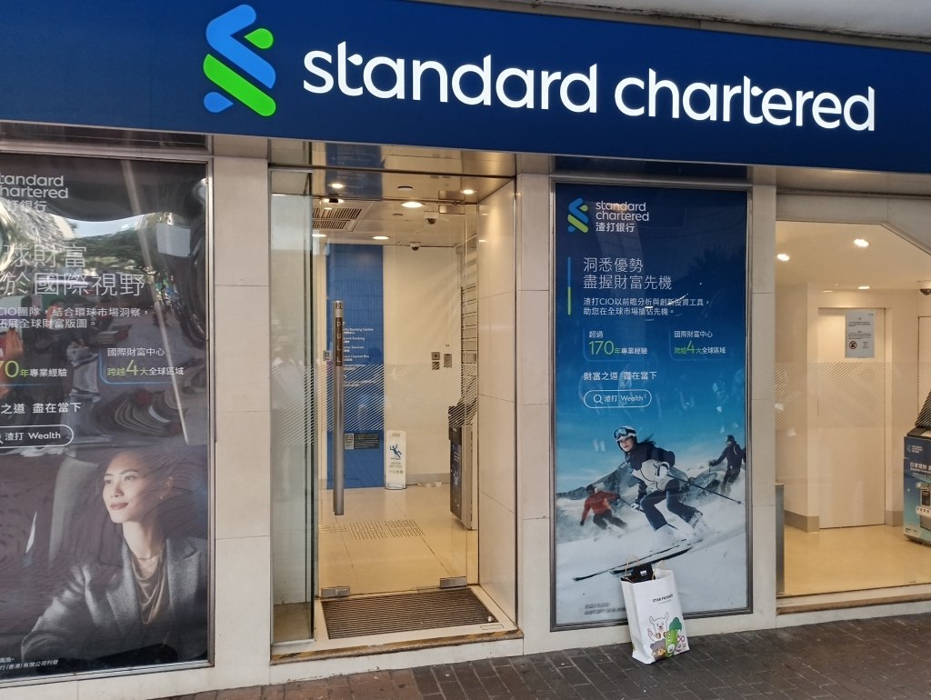 Blue Standard Chartered sign above glass entrance doors and window ads with Chinese text.